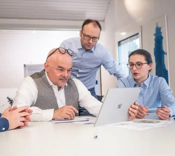 Two men and a woman sit around a laptop and discuss with interest.