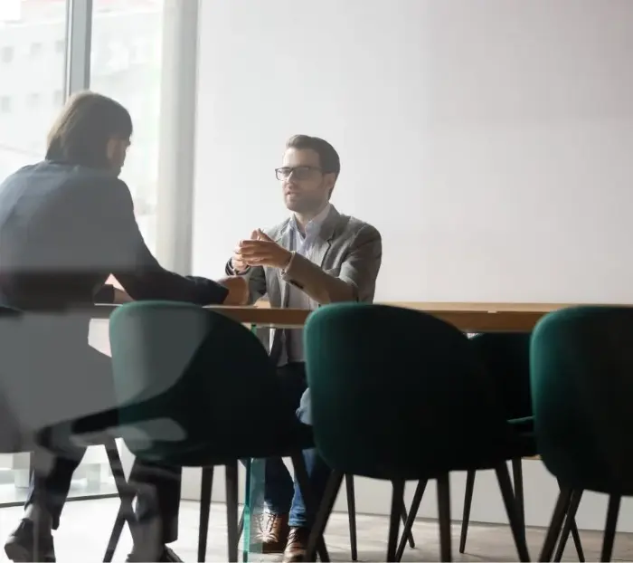 Two men sit across from each other at an office table and discuss things.