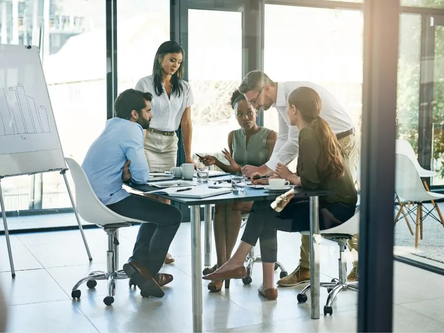 Five people sit and stand around a table in a meeting.