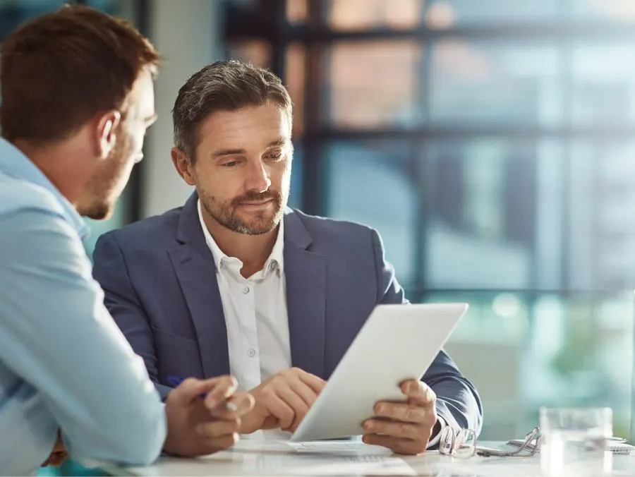 Two business people sit at a table and look at a tablet together. 