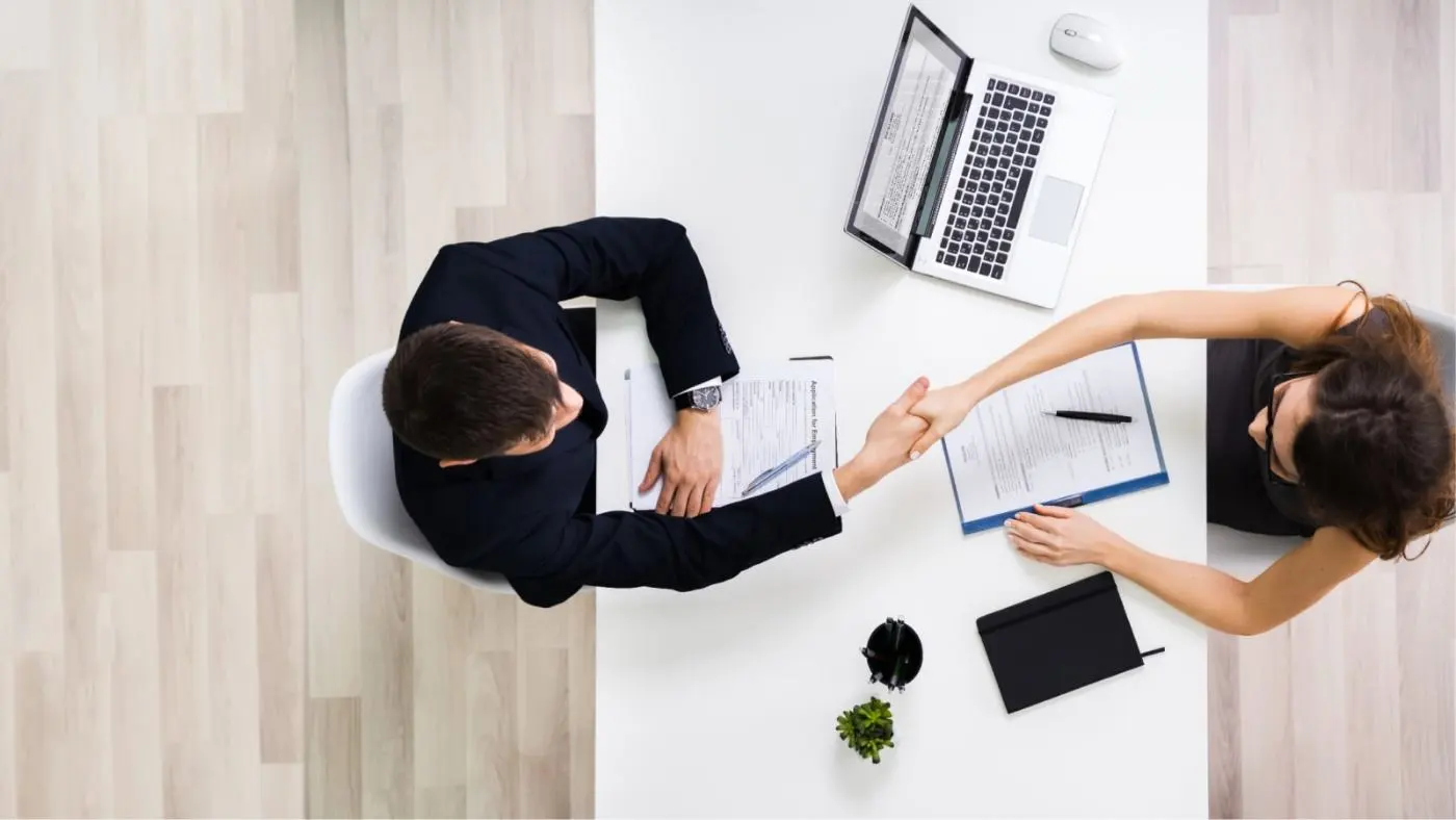 Bird's eye view of two people shaking hands at the table.