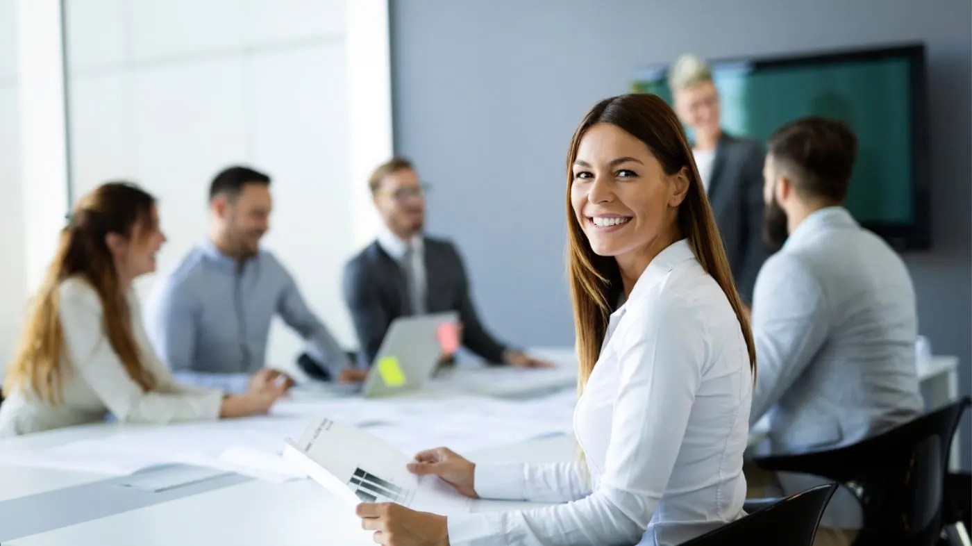 A woman smiles over her shoulder into the camera during a meeting.