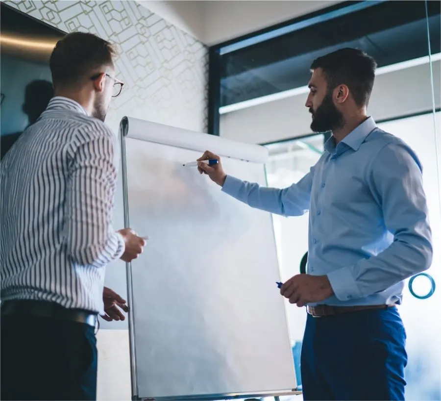 Two men stand in front of a whiteboard and discuss with each other.