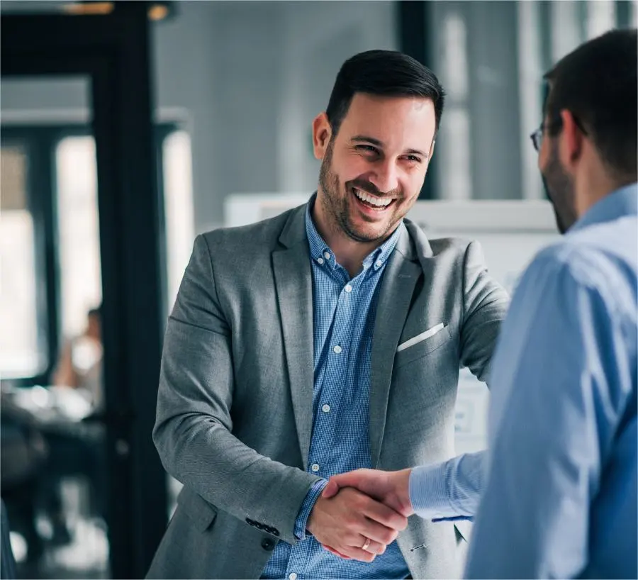 A smiling man in a suit shakes hands with another man.