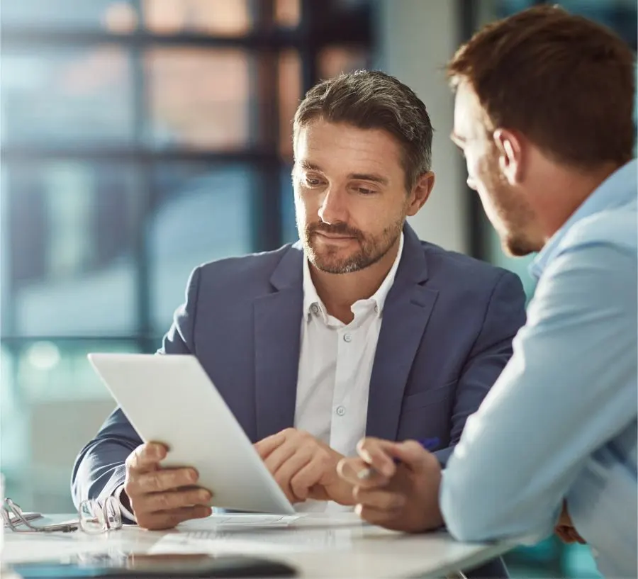 Two men in suits look at a tablet together and discuss.