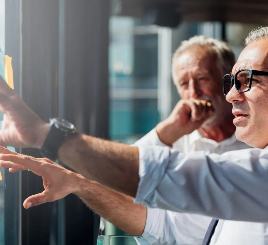 Two older men are deep in discussion about their notes on a glass wall.