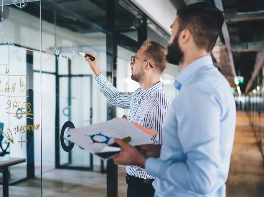 Two men are concentrating on taking notes on a glass wall.