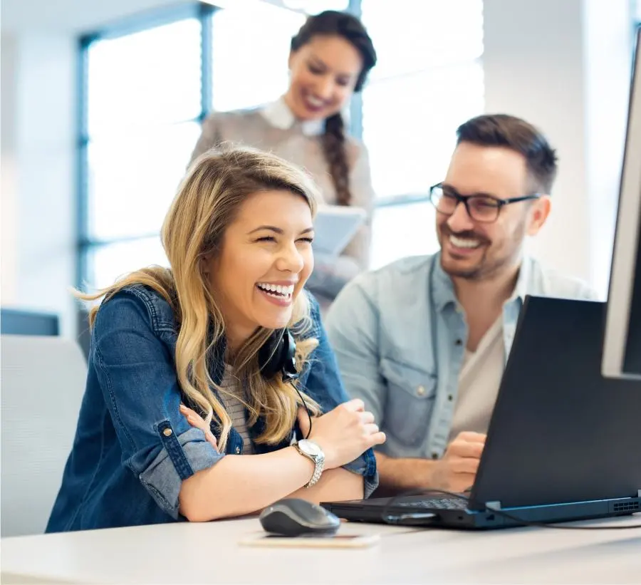 A woman and a man sit laughing in front of a computer.