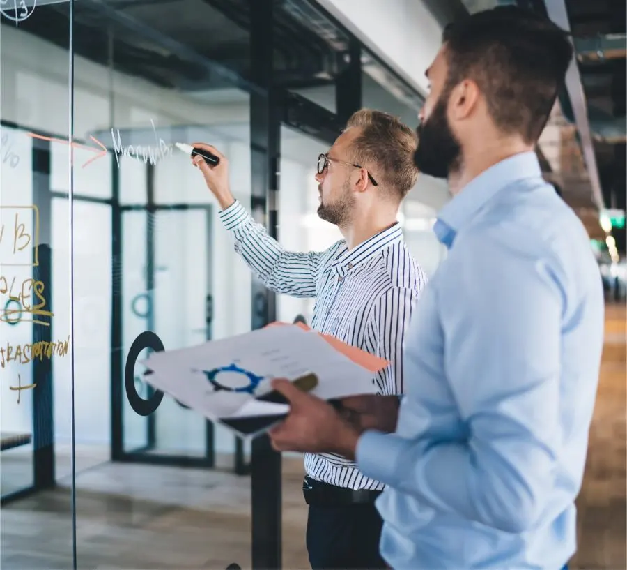 Two men are taking meeting notes on a glass wall.