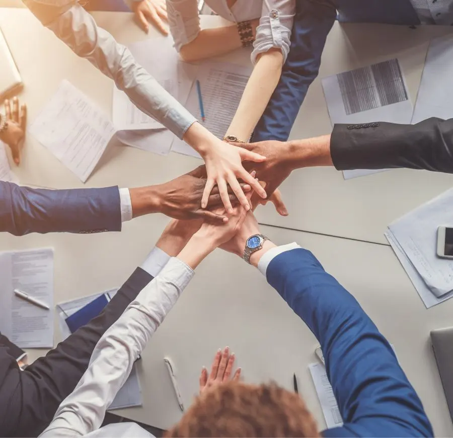 A business team stands in a circle and places their hands on top of each other in the middle to symbolize cohesion.