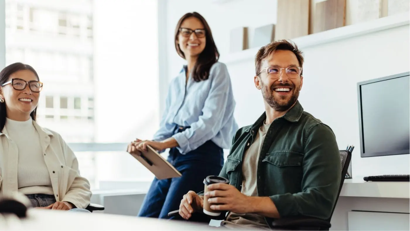 Three people in an office look out of the picture from the side, laughing.