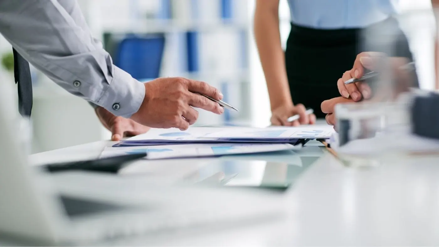 Three people are discussing documents lying on the table in front of them.