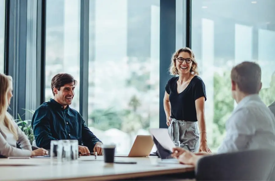 Picture of a standing laughing woman and a seated laughing man during a meeting with a view of the countryside.